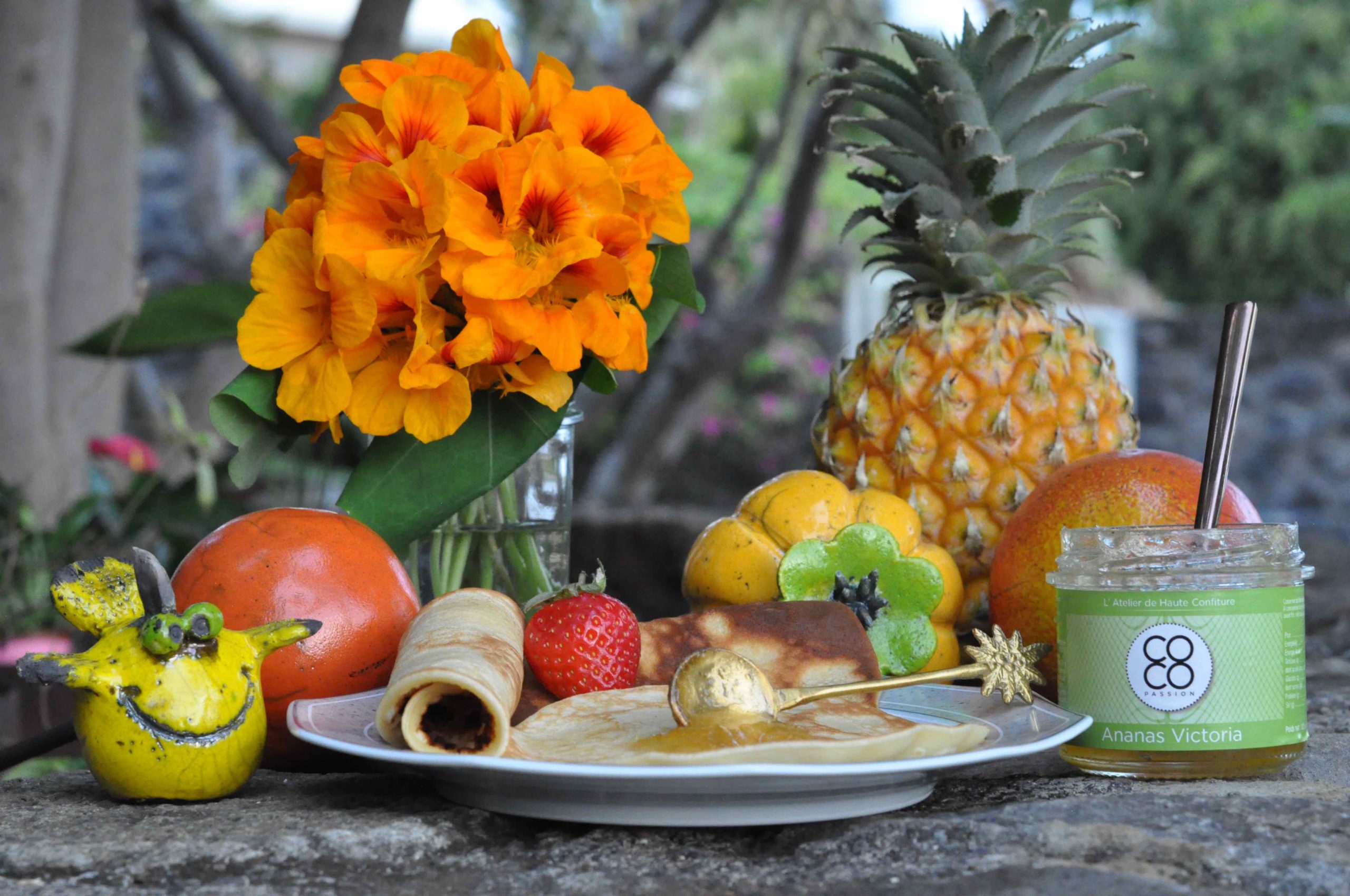 Table dressée avec un pot de confiture Ananas Victoria, des crêpes et des fruits de l'île
