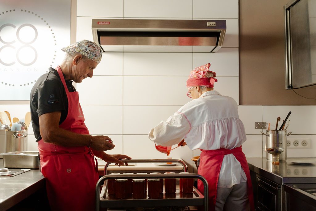 Une louche de confiture versée dans un pot, au-dessus du chaudron de cuivre de l'atelier
