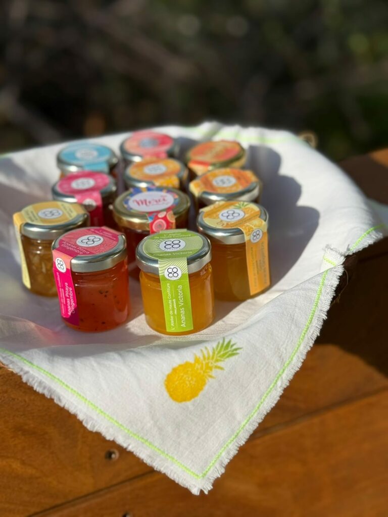Petits pots de confiture de parfums et de couleurs différents posés sur un torchon brodé d'un ananas
