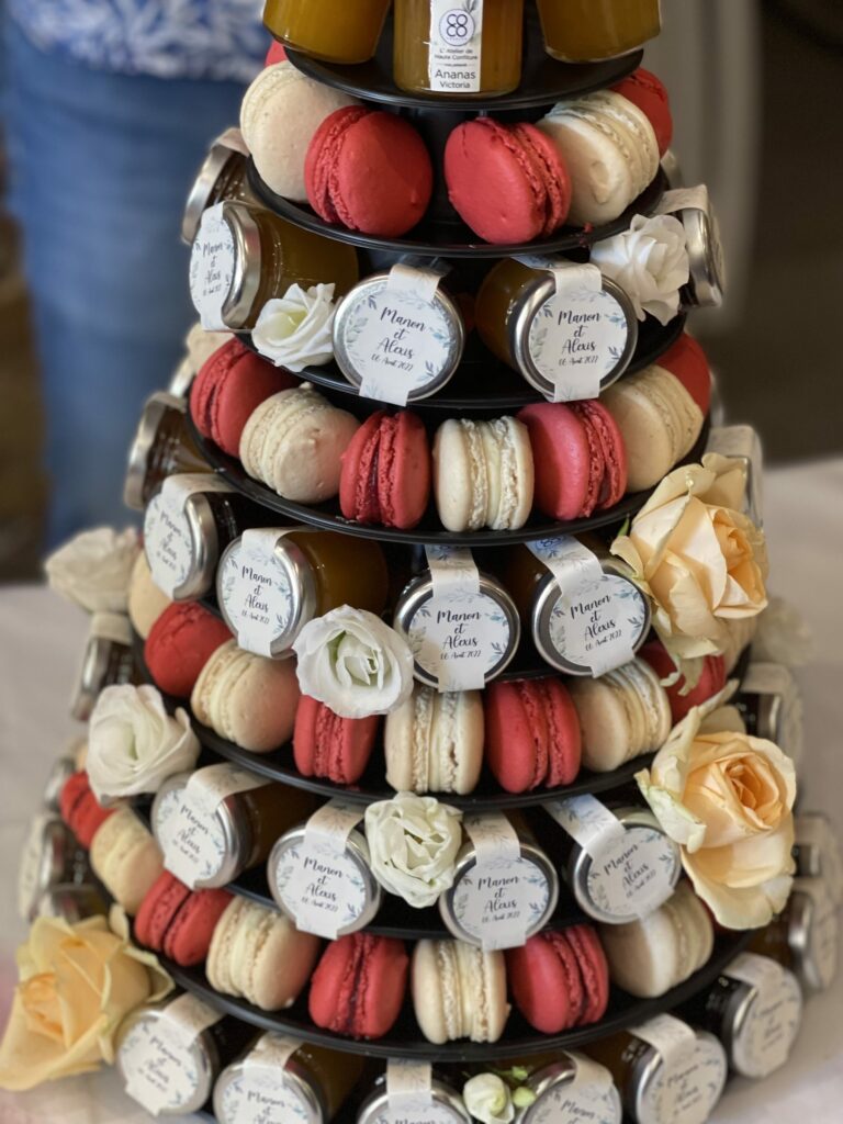 Pièce montée de macarons et de roses où sont glissés des petits pots de confiture personnalisés pour un mariage