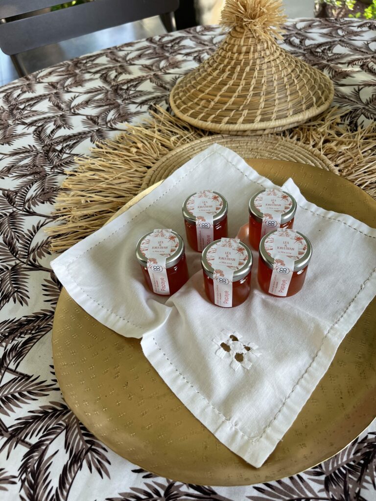 Cinq petits pots de confiture personnalisés posés sur une serviette brodée, sur une table dressée